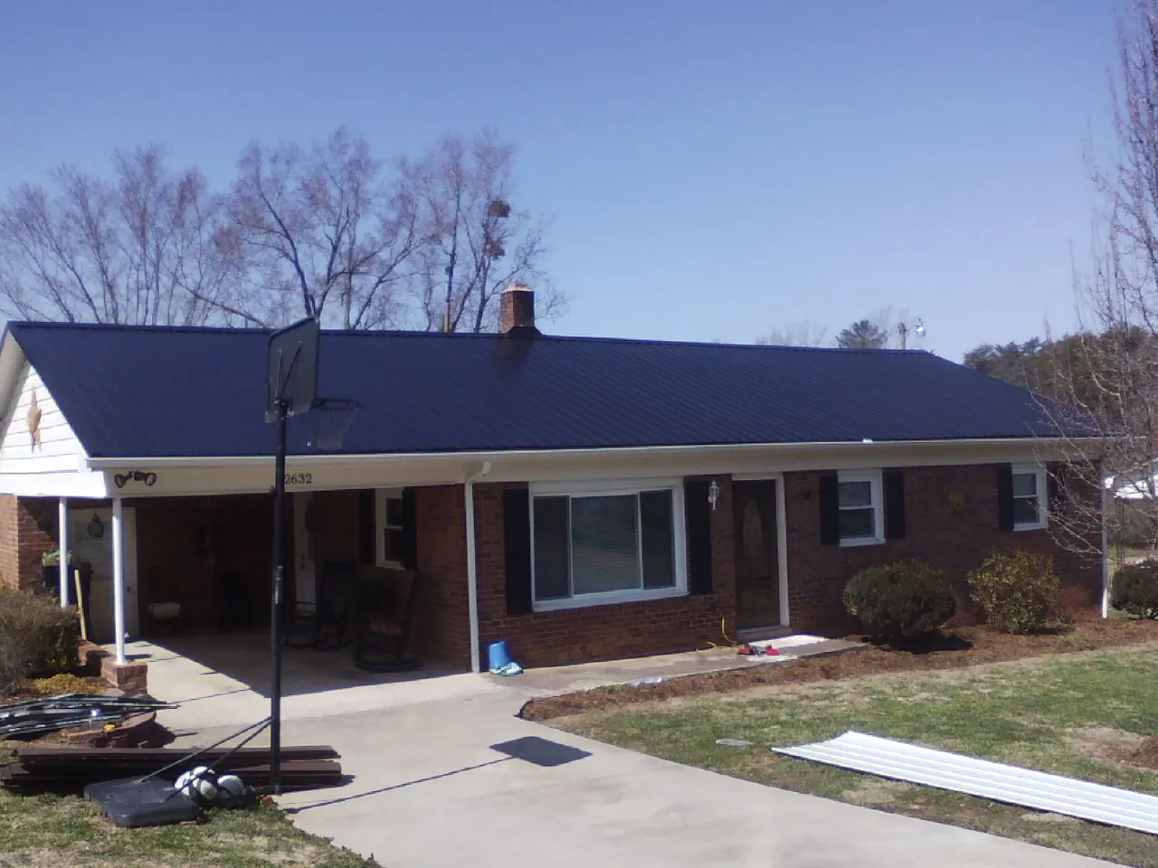 Finished dark blue metal roof on a brick ranch with a carport in Trinity